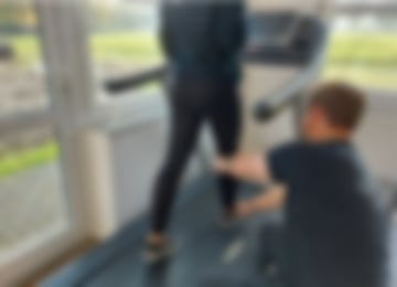 Eine Frau geht auf einem Laufband. Ein Therapeut kniet daneben und achtet auf den richtigen Gang