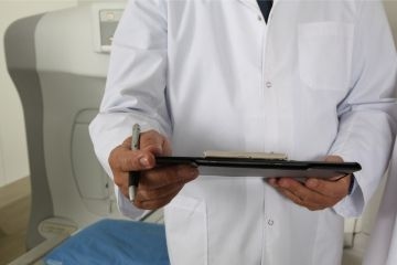 Ein Arzt in weißem Kittel hält ein Brett und einen Kugelschreiber