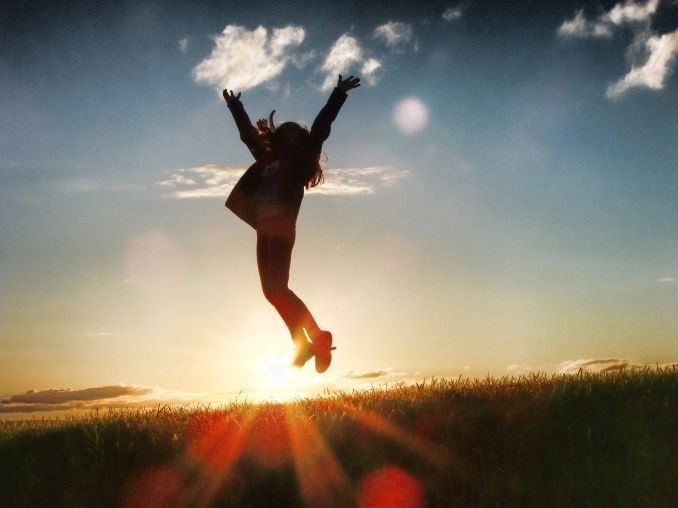 Eine Frau springt vor dem Sonnenuntergang in die Luft und streckt beide Arme in die Luft