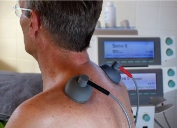 Ein Mann hat auf dem Rücken zwei Elektroden, im Hintergrund sind Geräte angeschlossen