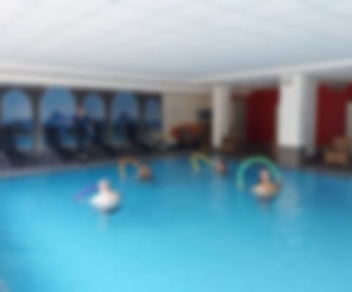 Ein Waserkurs im Sole-Thermalschwimmbad des MediVital Therapiezentrums. Die Trainerin steht am Beckenrand und zeigt den 4 Teilnehmern im Wasser Übungen mit einer Schwimmnudel, die Teilnehmer machen die Übungen nach