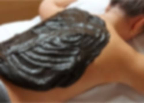 Eine Frau liegt auf einer Liege, auf ihrem Rücken hat sie eine dicke Moorpackung