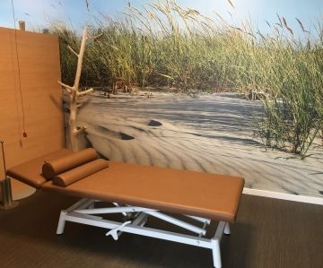 Eine Liege in der Physiotherapie im MediVital Therapiezentrum. Der Hintergrund an der Wand stellt eine Dünenlandschaft dar