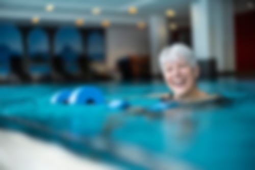 Eine Frau mittleren Alters mit kurzen grauen Haaren im Wasser mit einer Schaumstoffhantel.