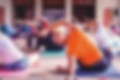 Eine Gruppe Sportler sitzen auf einer Trainingsmatte und machen eine Übung in einem Kursraum
