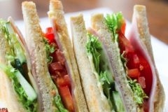 Mehrere Scheiben Sandwich, belegt mit Salat, Gurken, Tomate, Käse und Schinken.
