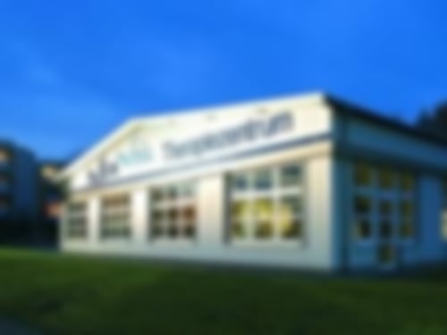 Das MediVital Therapiezentrum von außen am Abend. Durch die großen Fenster kann man auf das MTT schauen, im Hintergrund ist die Klinik Solequelle zu sehen.