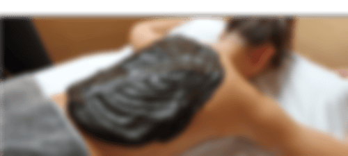 Eine Frau liegt auf dem Bauch auf einer Liege und hat eine Naturmoor Großpackung auf den Rücken.