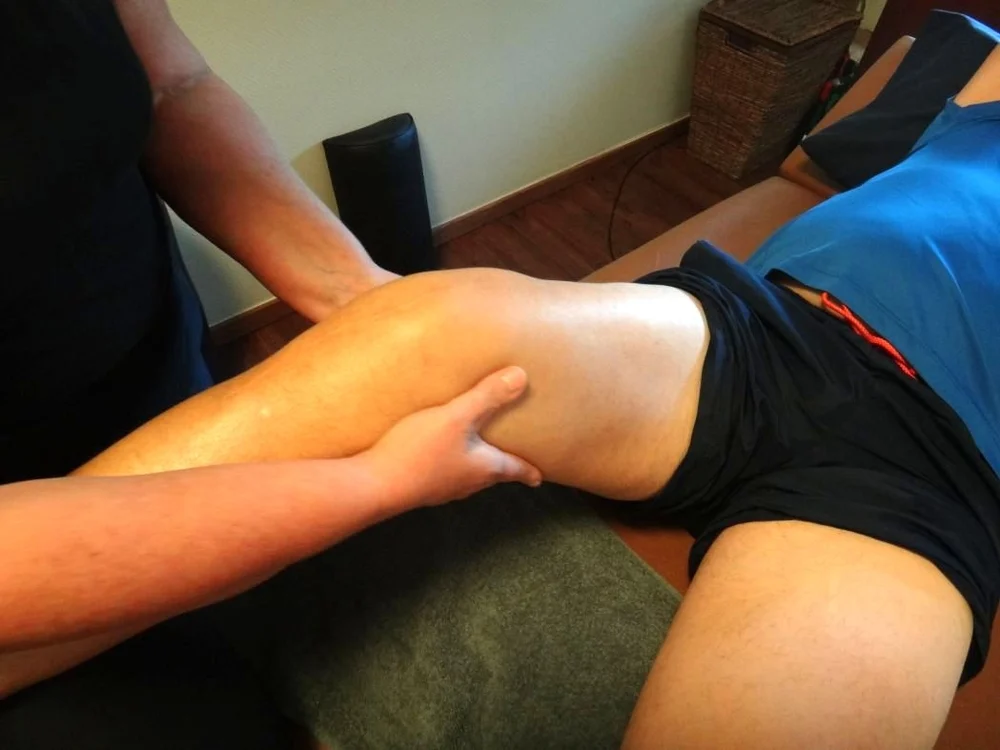 Das Knie eines Patienten, der auf einer Liege liegt, wird von einem Therapeuten massiert.