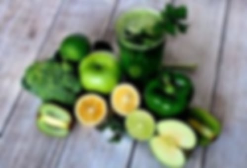 Äpfel, Kiwi, Zitrone, Limette, Paprika und ein grünes Glas Smoothie liegen auf einem Holztisch