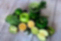 Äpfel, Kiwi, Zitrone, Limette, Paprika und ein grünes Glas Smoothie liegen  auf einem Holztisch