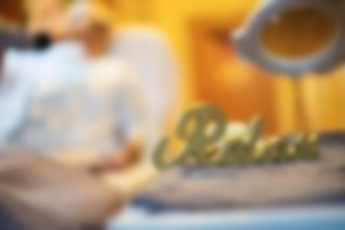 Der Dekoschriftzug "Relax" steht im Vordergrund. Dahinter erhält eine Patientin eine Kosmetik- / Wellnessanwendung.