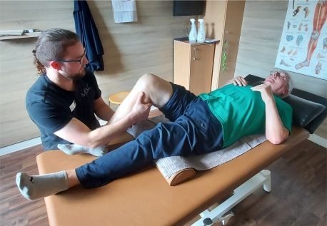 Ein Patient liegt auf einer Behandlungsliege und wird von einem Physiotherapeuten am aufgestellten Knie therapiert