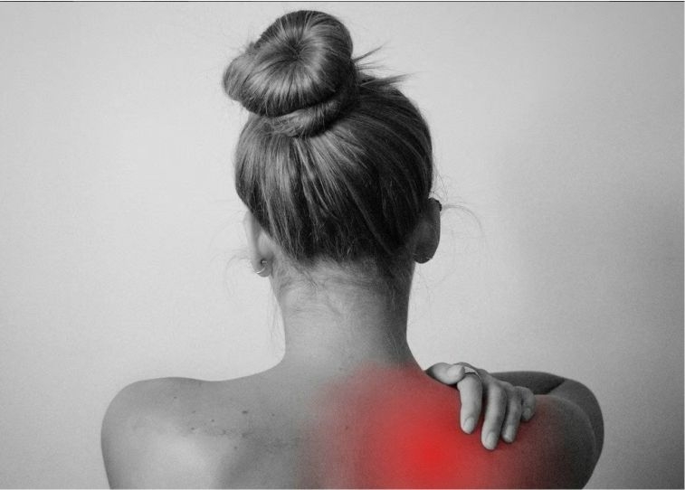 Eine Frau mit bloßen Oberkörper und hochgesteckten Haaren hält sich eine Hand auf ihre Schmerzende Schulter.