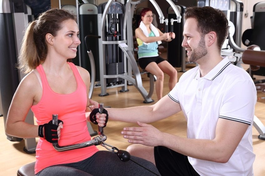 Eine Frau am Rudergerät von Technogym wird von einem Trainer angeleitet zur Übung