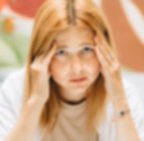 Eine Frau mit roten langen Haaren hält sich beide Hände an die Schläfen und sieht erschöpft aus.