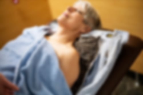 Eine Frau mittleren alters mit kurzen grauen Haaren liegt auf einer Moorpackung auf einer Behandlungsliege.