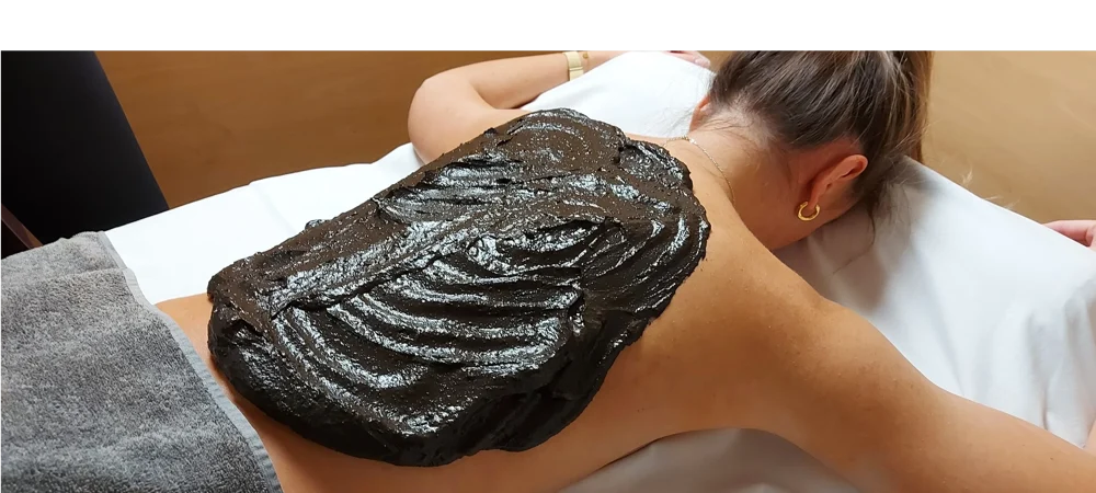Eine Frau liegt auf dem Bauch auf einer Liege und hat eine Naturmoor Großpackung auf den Rücken.