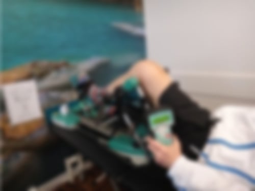 Ein Patient liegt auf einer Behandlungsliege und bekommt eine Therapie an einer Motorschiene für sein Knie