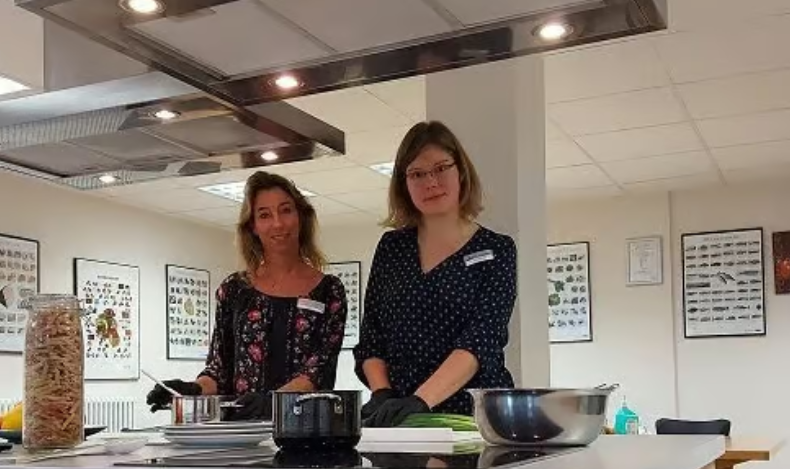2 Ernährungsberaterinnen der Klinik Solequelle stehen in einer Lehrküche am Herd und schauen in die Kamera