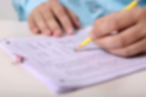 2 Hände liegen auf einem Tisch vor ein paar Blättern Papier. Eine Hand hält einen Stift.