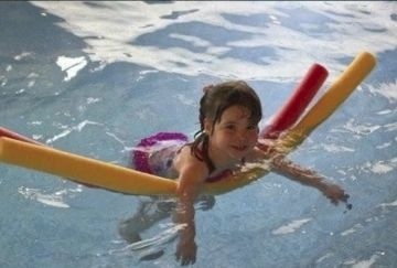 Ein kleines Mädchen schwimmt mit Hilfe zweier Schwimmnudeln im Wasser.