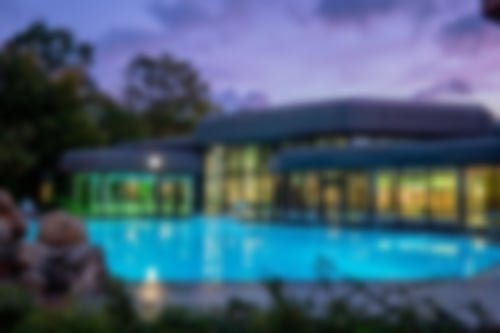 Außenansicht der Hellweg-Sole-Thermen. Im Vordergrund ist das Außenbecken zu sehen. In der Therme brennt Licht.