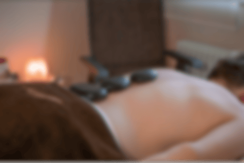 Ein Mann liegt auf einer Liege und entspannt bei einer Hot-Stone Massage. Die warmen Steine liegen auf seinem Rücken. Im Hintergrund leuchtet ein Salzkristall und sorgt für Gemütlichkeit.