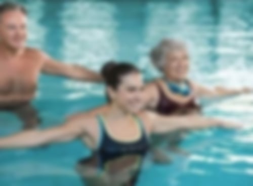 Zwei Frauen und ein Mann führen Übungen im Wasser durch. Dabei breiten sie ihre Arme aus.