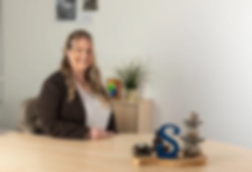 Simone Ruhnau, Fachfrau für Finanzen, sitzt an ihrem Schreibtisch im Büro und lächelt in die Kamera – unabhängige Finanz- und Versicherungsberatung