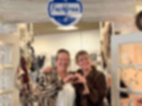 Simone Ruhnau und ihre Kollegin Gabi Funke stehen im Eingang zur Fachfrau. Sie formen mit ihren Händen ein Herz und lächeln in die Kamera.