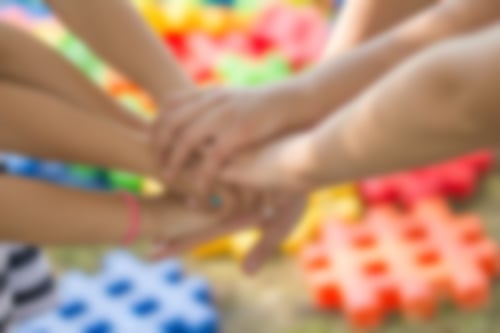 Hände treffen sich in der Mitte. Im Hintergrund bunte Bausteine