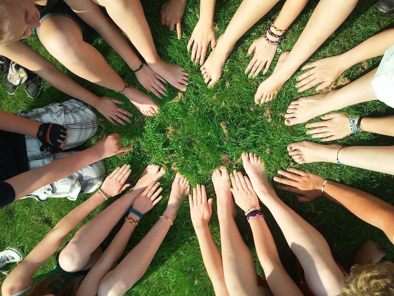 viele Hände und Füße bilden auf grünem Gras einen Kreis