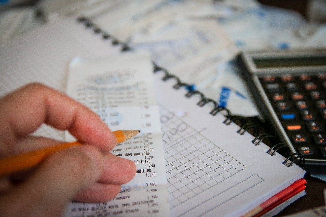 Quittung, Block, Taschenrechner. Im Vordergrund Hand mit Bleistift