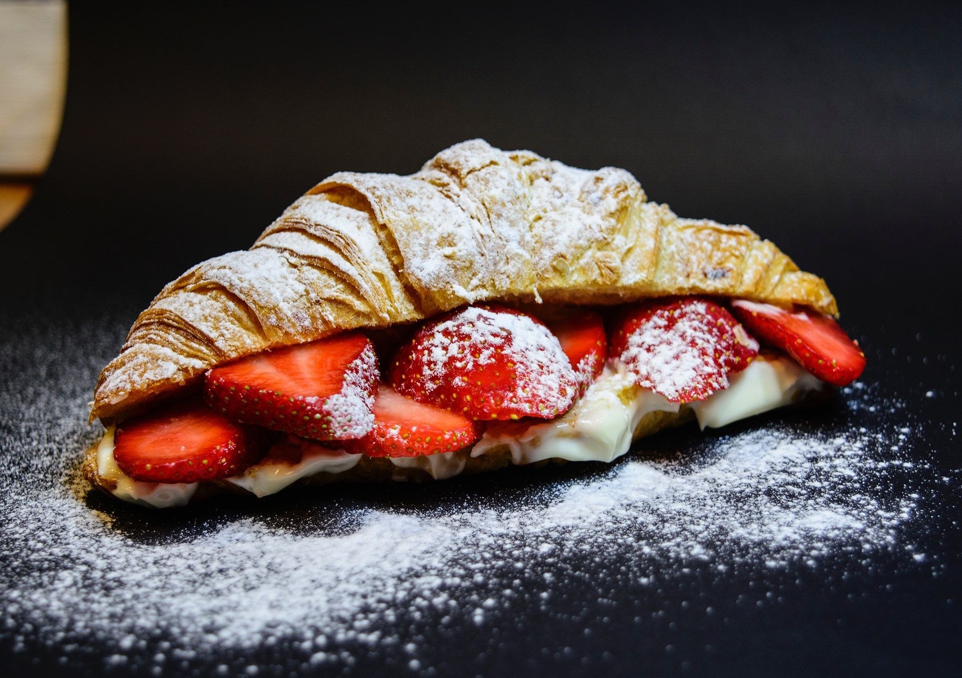 Zartes Croissant gefüllt mit griechischem Joghurt, frischen Erdbeerscheiben und bestäubt mit Puderzucker