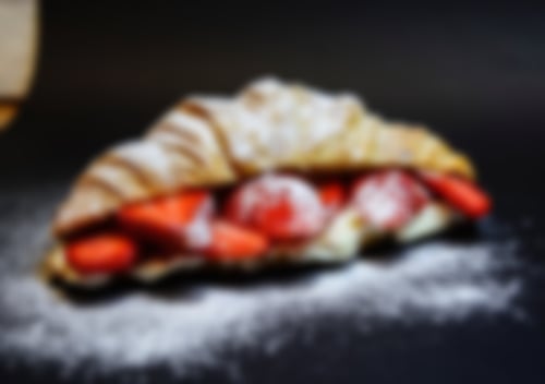 Zartes Croissant gefüllt mit griechischem Joghurt, frischen Erdbeerscheiben und bestäubt mit Puderzucker