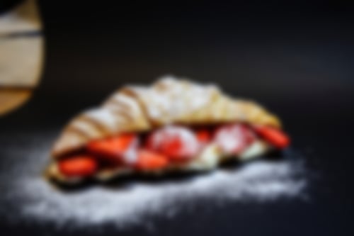 Buttercroissant gefüllt mit frischen Erdbeerscheiben und cremigem Joghurt, bestäubt mit Puderzucker auf dunklem Untergrund