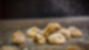 Nahaufnahme von kleinen Plätzchen mit Schokostücken, die mit Puderzucker bestäubt werden, auf einem Backblech.