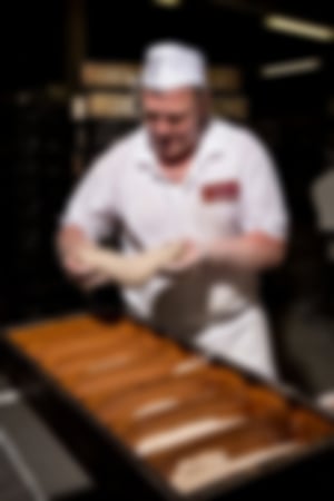 Bäcker in Essmann’s Backstube-Uniform formt Brotteig per Hand und legt ihn in große Brotbackformen.