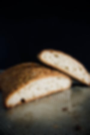 Frisches, aufgeschnittenes Sauerteigbrot mit knuspriger Sesamkruste, das auf einem gelochten Backblech liegt, vor dunklem Hintergrund.