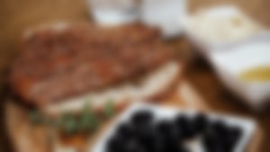 Sesambrot in Scheiben geschnitten, angerichtet auf einem Holzbrett mit schwarzen Oliven, Olivenöl und Dips.