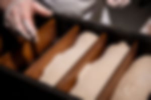 Bäcker in Essmann’s Backstube-Uniform arbeitet mit Brotteig, umgeben von Brotformen und moderner Backtechnik im Hintergrund.