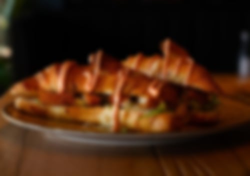 Herzhaft belegtes Croissant mit knusprigen Fischstäbchen, frischem Salat und würziger Sauce