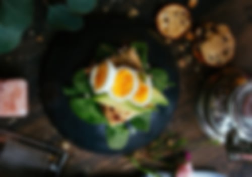 Rustikales Bauernbrot mit Frischkäse, Avocadoscheiben, Babyspinat und weichgekochtem Ei, garniert mit Pfeffer und Kräutern