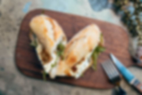 Knuspriges Baguette belegt mit cremigem Camembert, Rucola und karamellisierten Walnüssen auf Holzbrett serviert