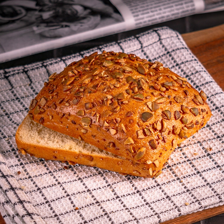 Herzhaftes Dinkelbrötchen mit goldbrauner Kruste, üppig bestreut mit gerösteten Kürbiskernen bei Essmann’s Backstube