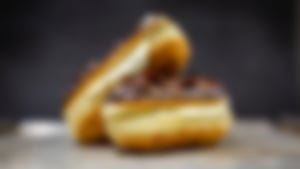 Zwei Eclairs mit Schokoladenglasur und Sahnefüllung, dekorativ auf einem Backblech arrangiert, Nahaufnahme.