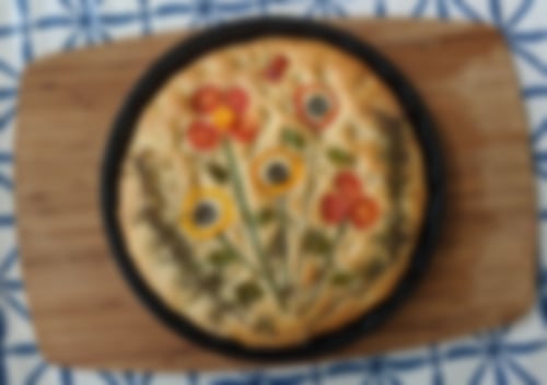 Goldbraune Focaccia mit kunstvoll arrangiertem Gemüsedekor aus Tomaten, Paprika, Oliven und Kräutern