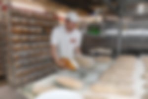 Bäcker in Essmann’s Backstube-Uniform arbeitet mit Brotteig, umgeben von Brotformen und moderner Backtechnik im Hintergrund.