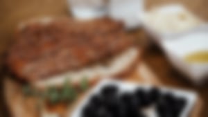 Sesambrot in Scheiben geschnitten, angerichtet auf einem Holzbrett mit schwarzen Oliven, Olivenöl und Dips.